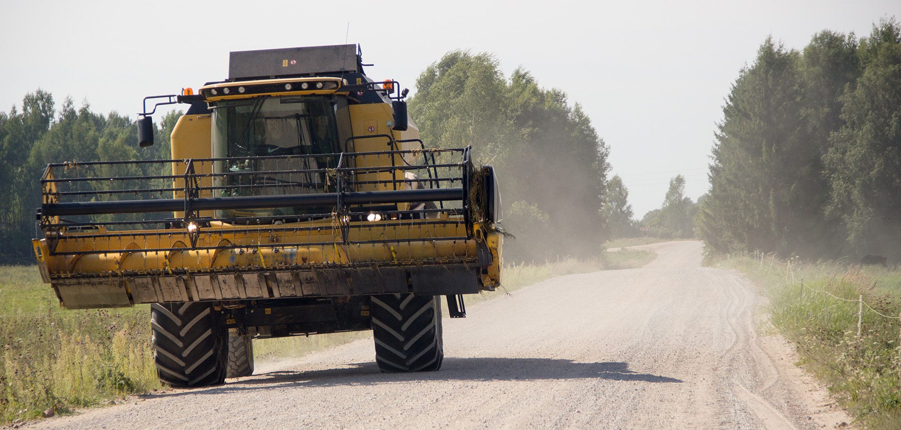 Large farm equipment traveling down a narrow gravel road.