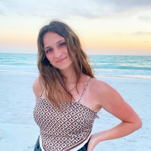 woman standing in front of ocean posting for portrait with long brown hair and tank top with geometric print