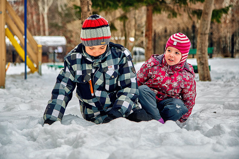 A boy and girl wearing winter coats and stocking caps playing in the snow.