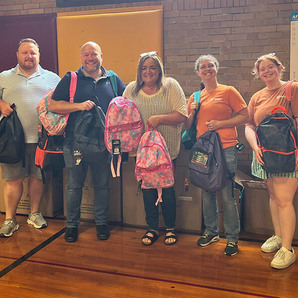 The team at Onward Injury Law stands with the school faculty inside the gymnasium holding up the backpacks they just donated to the school in Bloomington, IL.