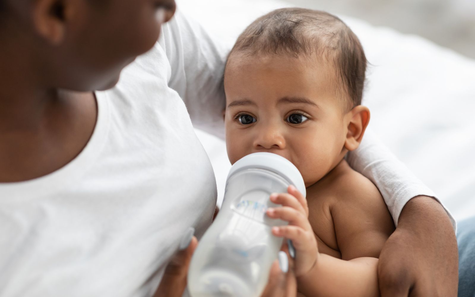 Infant is being fed a bottle by an adult woman, likely his mother.