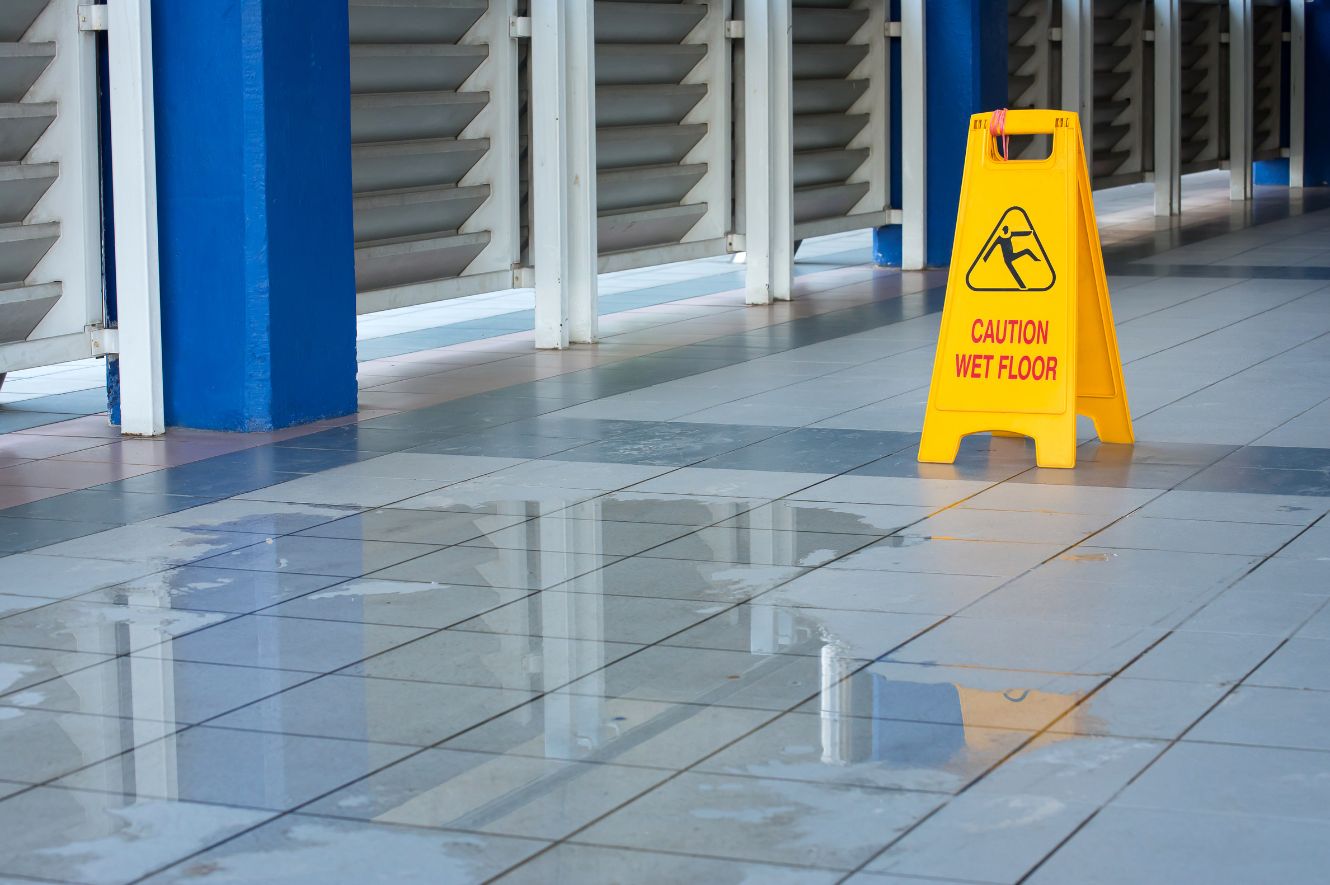 Hallway that has water on the floor with a Wet Floor sign nearby.