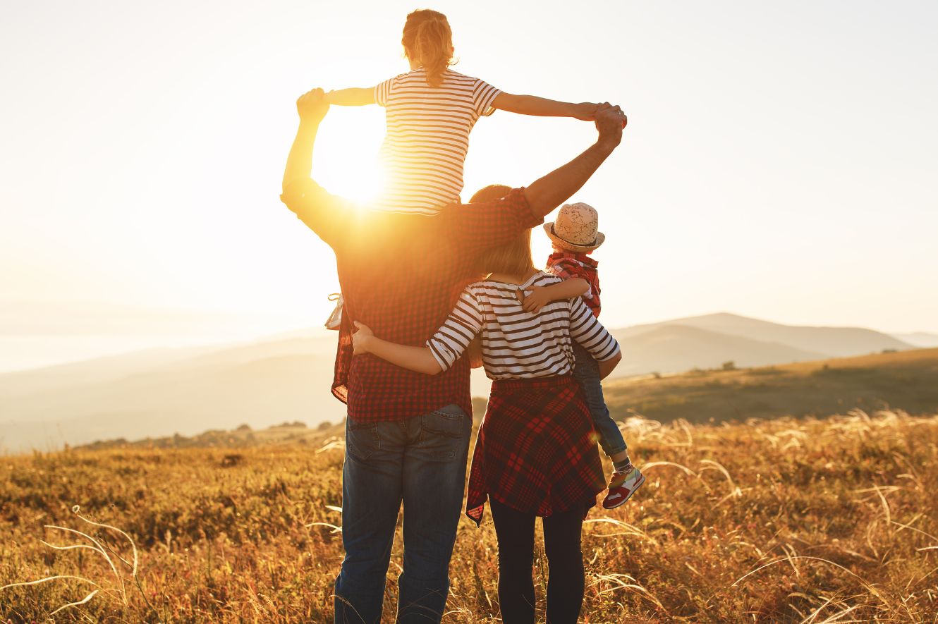 A couple standing with their children looking off into the sunset.