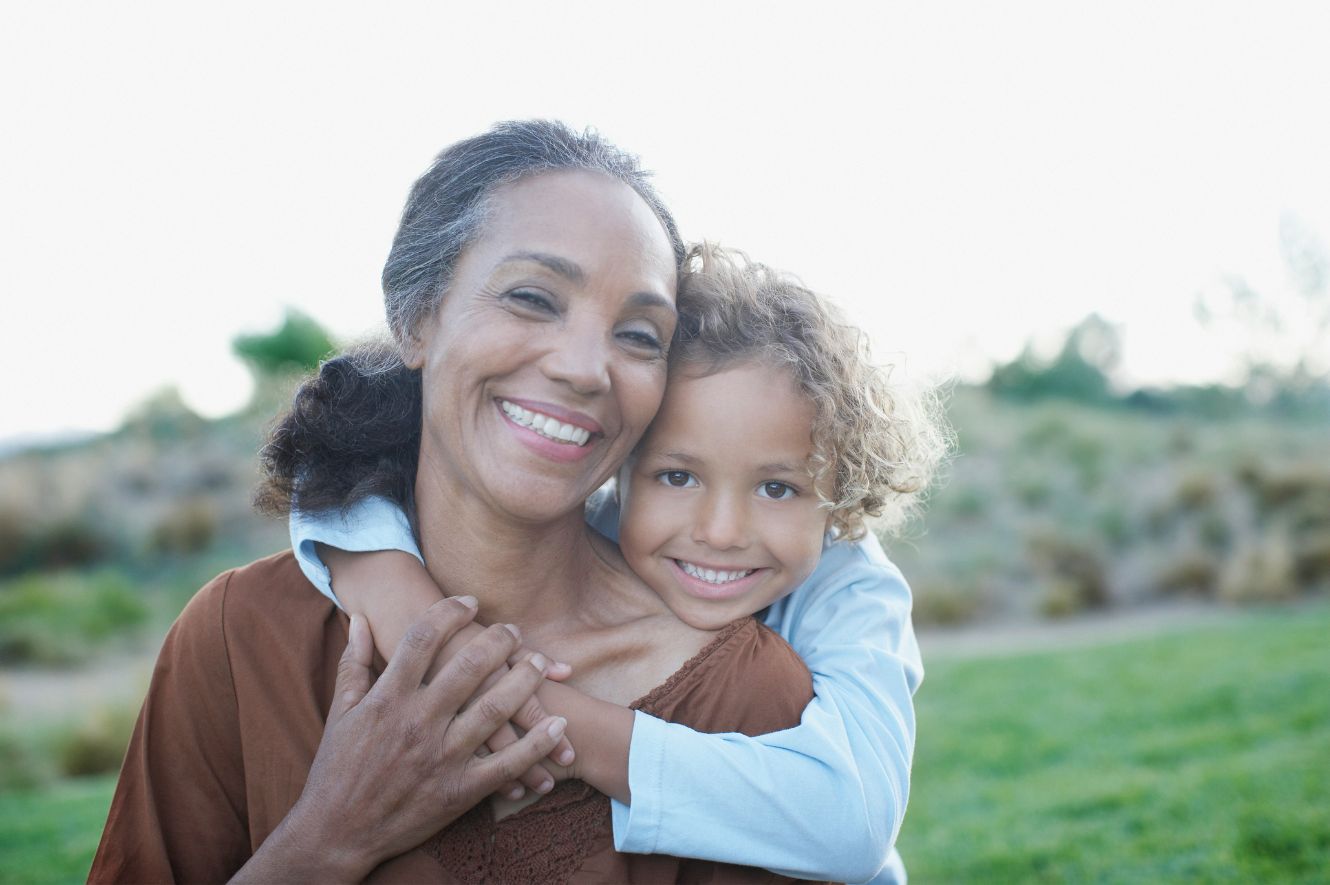 Image of middle aged woman smiling at camera with young child hugging her