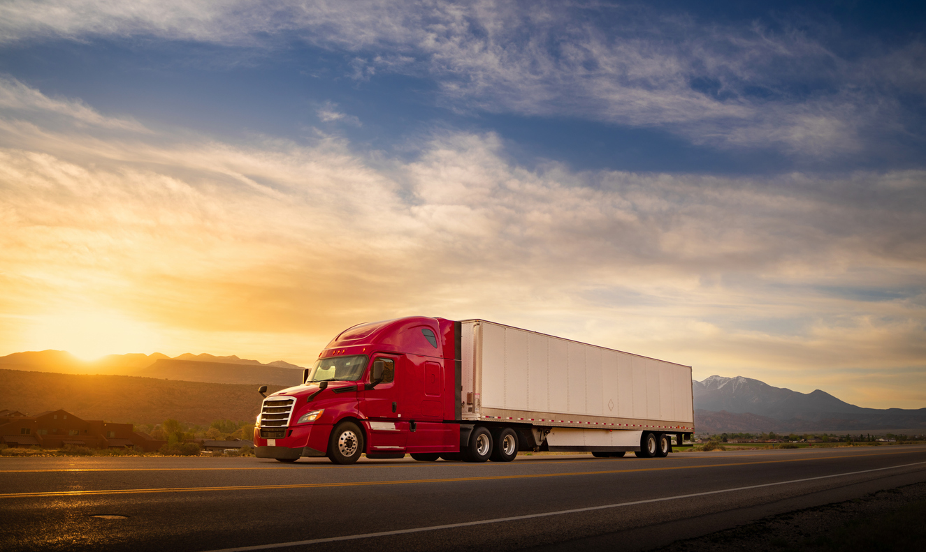 Red and white semi-truck speeding at sunrise