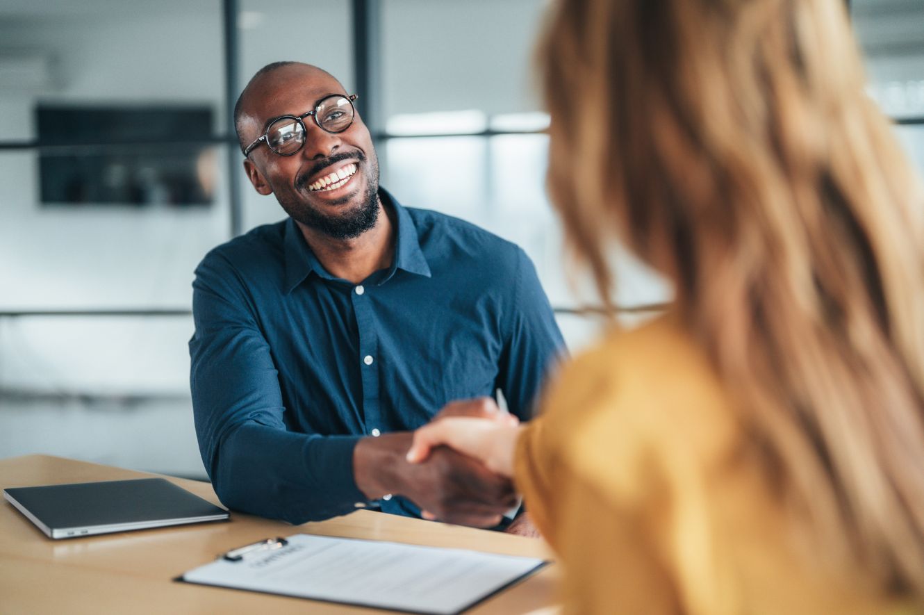 middle aged man shakes hands with woman at desk after signing an insurance policy